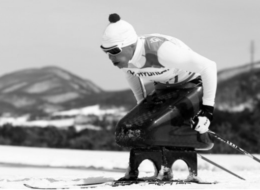 Sitz-Skiläufer im Rennanzug und Skibrille auf Sit-Ski, unterwegs auf verschneiter Strecke vor Bergen